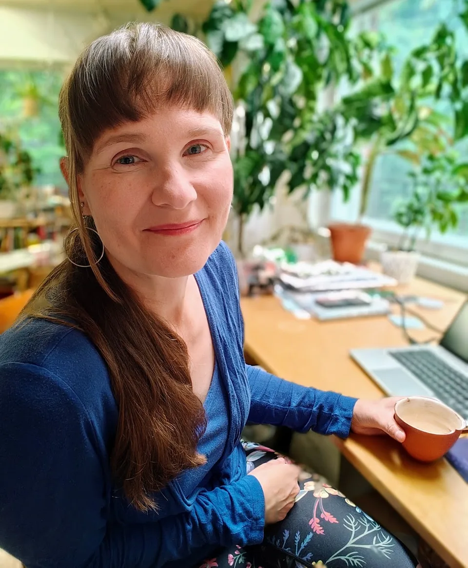Satu Kulovesi-Kilpinen työpöytänsä ääressä kahvikuppi kädessä.
